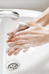 Hand Washing in white sink. Water flows from a faucet at soapy female hands. Covid-19 coronavirus protective measure.