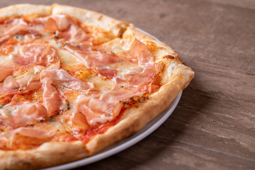 details of fresh baked pizza with ham on a wooden table