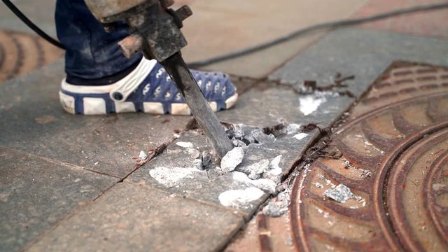 A jackhammer worker smashes a marble slab around an iron hatch