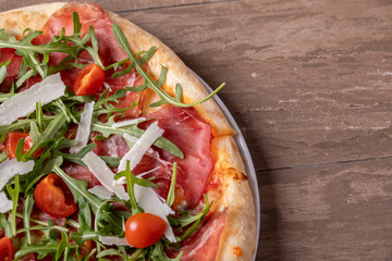 close up of delicious italian fresh pizza with ham, arugula, tomato and parmesan