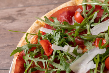 close up of delicious italian fresh pizza with ham, arugula, tomato and parmesan