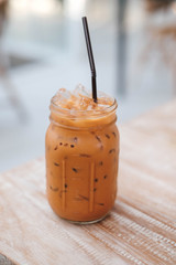 Iced Thai Milk Tea in glass with straw on wooden table in cafe.