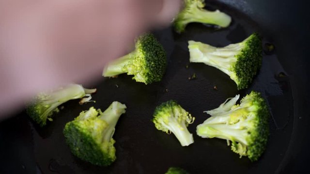 Close up of an egg falling into a frying pan and cooking with broccoli