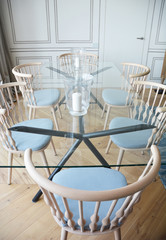 A modern tempered glass rectangular dining table with stainless steel cross legs and blue admiral armchairs with wood backs.