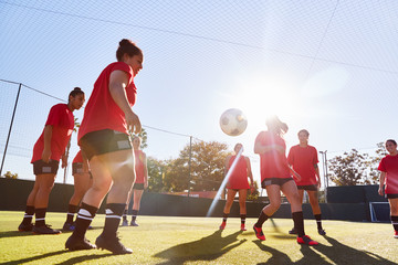 Womens Football Team Kicking Ball Whilst Training For Soccer Match On Outdoor Astro Turf Pitch