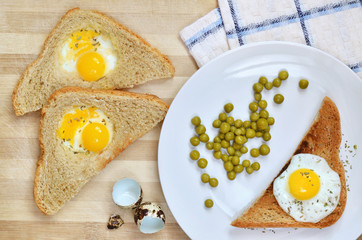 Toasts with fried quail eggs and green peas on a white plate on a wooden cutting board, top view. Healthy food.