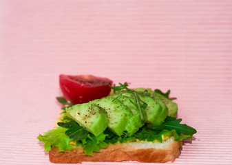 Pink background and square toast with avocado, cherry tomato, arugula and salad. Useful and delicious breakfast.
