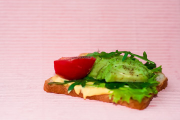 Pink background and square toast with avocado, cherry tomato, arugula and salad. Useful and delicious breakfast.