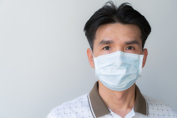 An Asian man wears a face mask on a gray background.