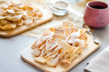 Homemade shortbread cookies with icing sugar on a wooden board with tea in a pink cup on a gray background in the sunlight. Side view