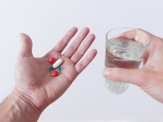 Close up of pills in hand with a glass of water