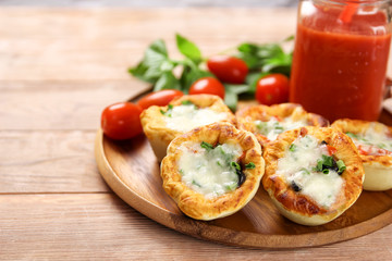  Small pizzas with mozzarella cheese, ham, olives and green onions on a wooden plate. With tomato juice in a glass jar on a natural kitchen table. Close-up.