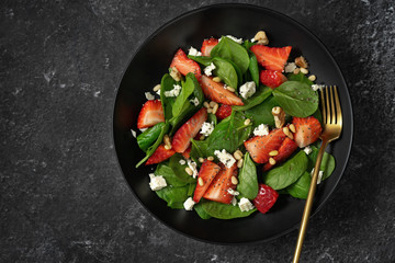 Top view of a plate with strawberry spinach salad on black background