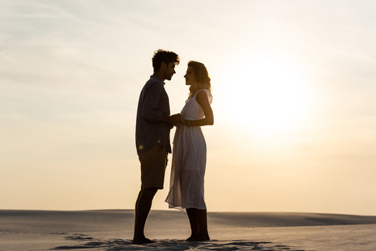 side view of young couple holding hands on sandy beach at sunset