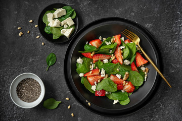 Top view of a black plate with strawberry spinach salad and its ingredients