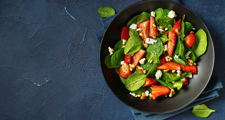 Close up of strawberry salad with spinach, feta ans nuts on classic blue background