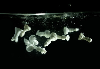 white color chess pieces dropping down in water creating water splash and bubbles amazing under...