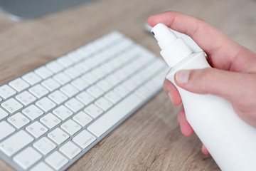 purity, coronavirus protection and disinfection concept - male hand cleaning keyboard with sanitizer spray