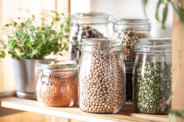 Set of different legumes in glass jars on, concrete white table. A source of protein for...