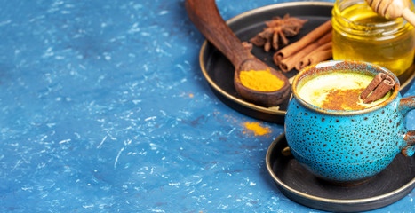 Blue cup of indian ayurvedic healthy drink - golden turmeric latte milk and plate with ingredients on blue. Copy space.