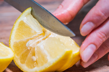Macro slicing a juicy lemon with a large knife on a wooden board. Healthy vegan food, Mexican...