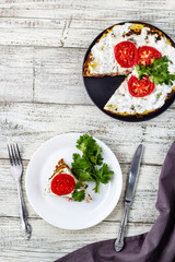 Zucchini cake with tomatoes and fresh parsley on white wooden background.