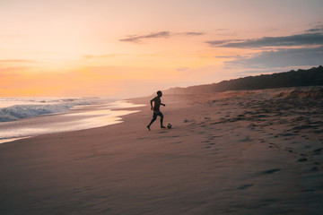 Silhouette of a man with a ball running on the sandy beach of the Pacific Ocean