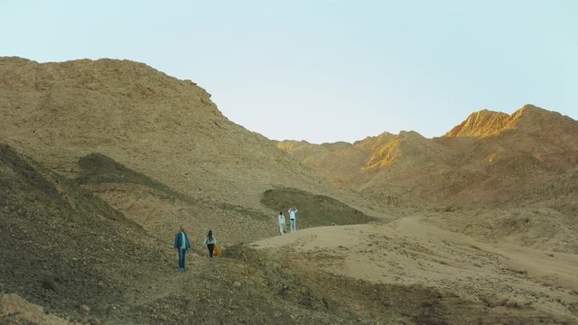 Group of tourist walk along the rock canyon in hot desert, tourists take picture and have fun. Desert mountains background, Egypt, Sinai, slow motion, 4k