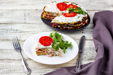 Zucchini cake with tomatoes and fresh parsley on white wooden background.