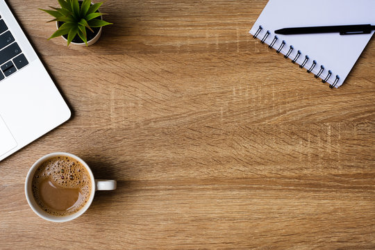 desk office with laptop, blank notepad, coffee cup and pen on wood table. Flat lay top view copy spce.