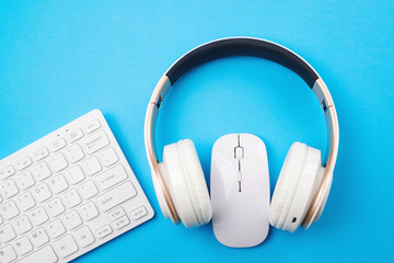 White keyboard, mouse and headphones on blue background, top view. Copy space. Remote education and...