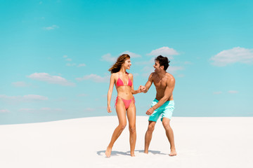 smiling young couple holding hands on sandy beach