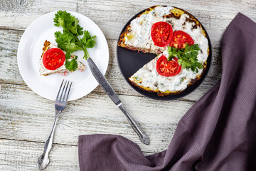 Zucchini cake with tomatoes and fresh parsley on white wooden background.