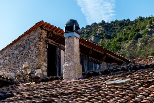 A close-up shot of a chimney on a rooftop with traditional French roof tiles with the cliff Alps mountains and blue clear sky in the background