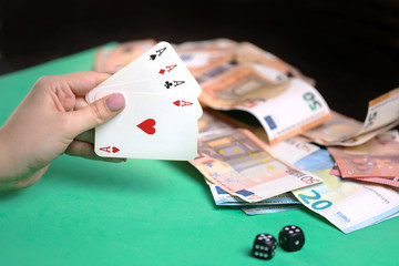 Hand with playing cards ,  game dice, money on the green poker table.  Gambling. Addiction