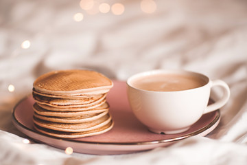 Stack of tasty pancakes with cup of coffee in bed closeup. Good morning. Breakfast time. Selective focus.