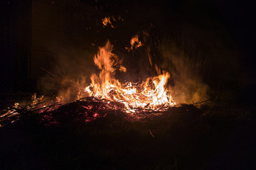 Bonfire on the street, burning branches and a tree, flame and sparks rise up.