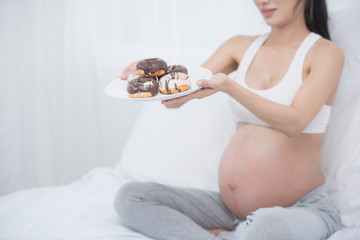 beautiful young pregnant woman holding sweet donut in her hand. expectation of the child, pregnancy and motherhood. healthy and unhealthy eating concept, diet. Junk food. soft focus background