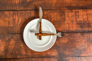 A fork and a knife with a wooden handle lie on a white plate in the form of a clock, the concept of eating by time.