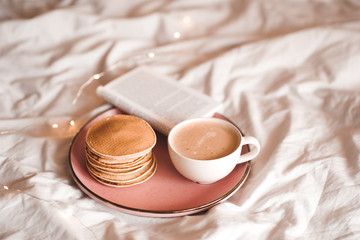 Pancakes with white cup of coffee and open paper book in bed closeup. Good morning. Breakfast time.