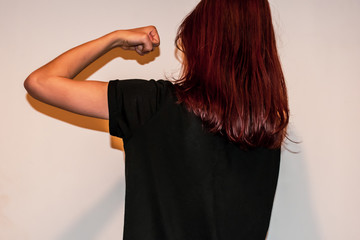 A back view close-up shot of a strong unrecognizable young Caucasian redhead woman showing her clenched fist up