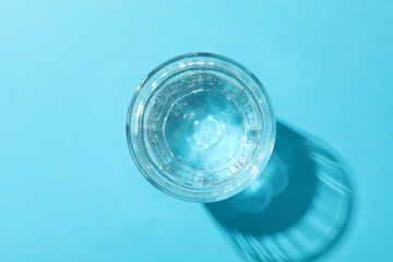 Glass of water on blue background, top view