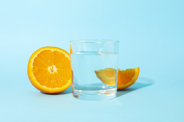 Orange and glass of water on blue background, close up