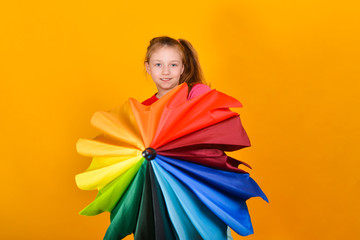 Obraz na płótnie Canvas A girl in a colored sweater holds a multi-colored umbrella in her hand on a yellow background, a child and the colors of the rainbow.