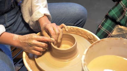 Boy and woman makes a pot with pottery wheel in a workshop