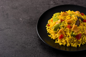 Fried rice with chicken and vegetables on black plate on black background. Copy space