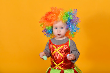 A small child, a girl in a clown wig, holds Easter eggs in her hands.