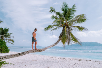 La Digue Seychelles, young men walking at the white beach with clear blue ocean on vacation at the tropical Island