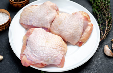 Raw chicken thighs in a white plate with spices on a stone background