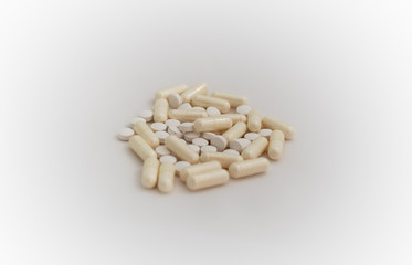 Bunch of pills - tablets and capsules - on white background. Selective focus. Light yellow capsules and white tablets are scattered over a white background. Virus cure.